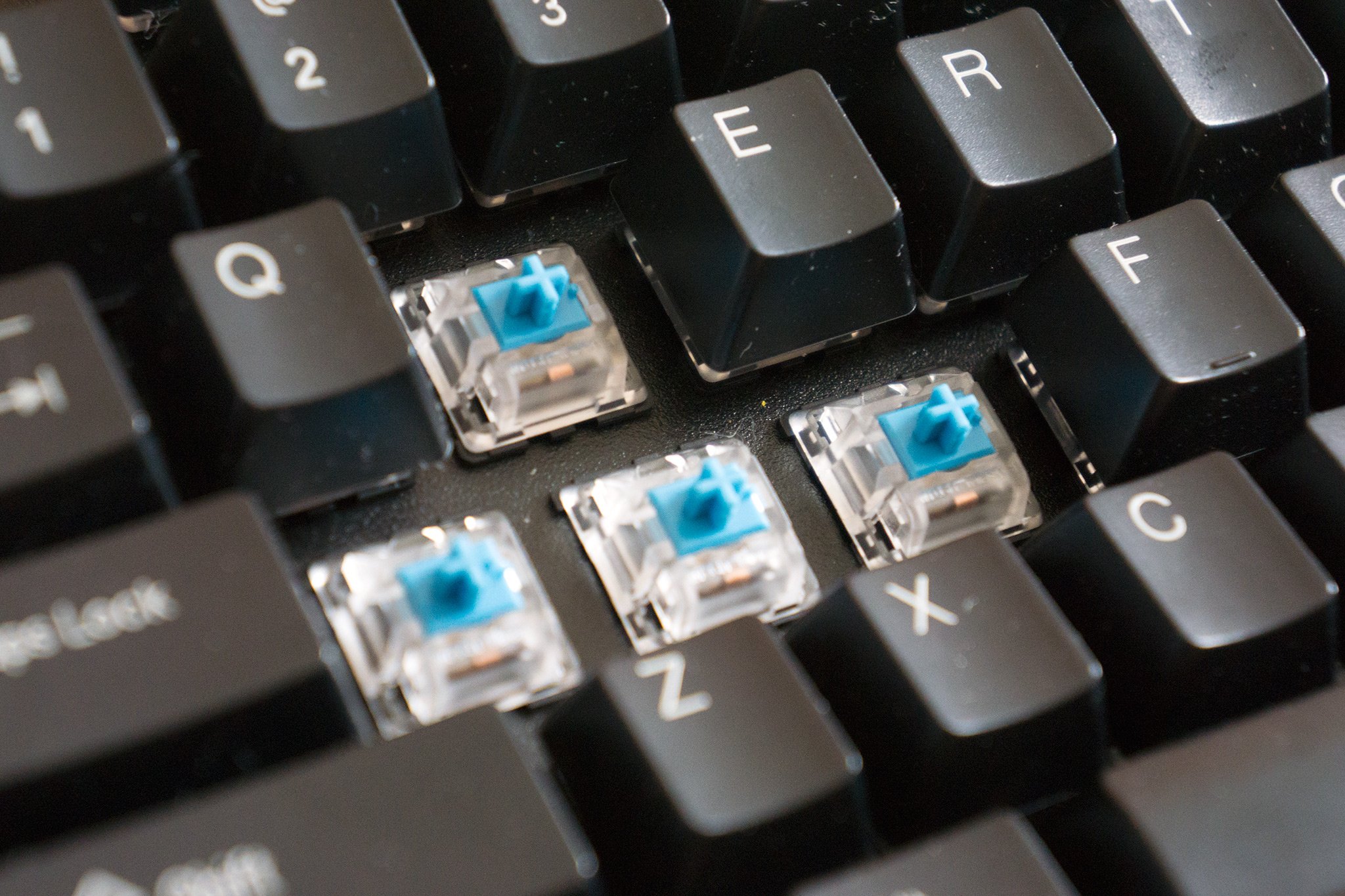 An image of a mechanical keyboard, with the W A S D keycaps removed to expose the blue switches in clear housing in the keyboard
